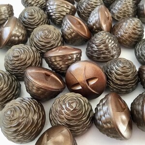 May include: A selection of brown decorative buttons. The buttons feature diverse designs, including spiral and geometric patterns. Crafted from a dark brown material, they are arranged on a white surface. These buttons are suitable for sewing projects.