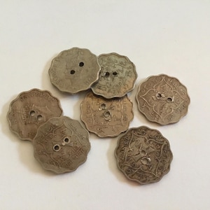 Op de afbeelding: Zes zilverkleurige knopen met ingewikkelde ontwerpen en twee gaten elk. De knopen hebben een licht verweerd uiterlijk.