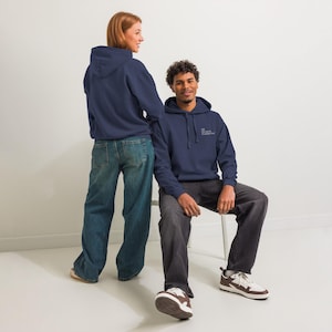 May include: Two people wearing navy blue hoodies and jeans. The hoodie on the right has the text "OK, but first, probably food" in white. The person on the right is sitting on a white chair.