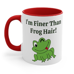 May include: White ceramic mug with a red rim and handle. The mug features a green cartoon frog with a tongue sticking out and the text "I'm Finer Than Frog Hair!"