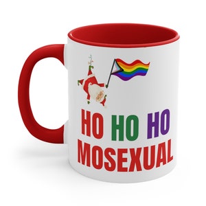 May include: White ceramic coffee mug with a red rim and handle. The mug features a cartoon image of Santa Claus holding a rainbow pride flag and the text "HO HO HO MOSEXUAL".