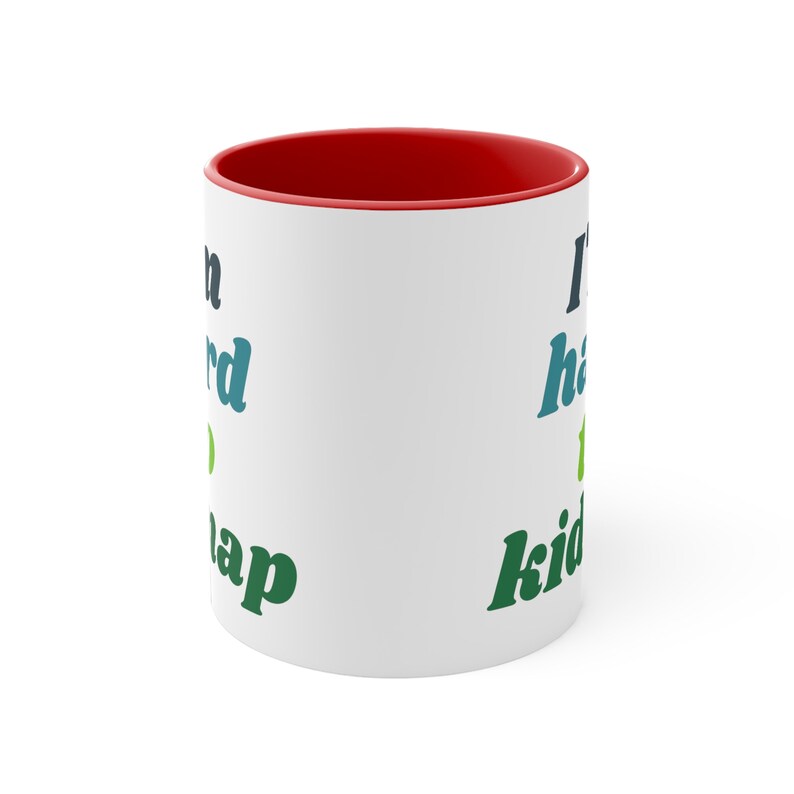 May include: White ceramic mug with a red rim. The mug has a green, blue, and black design with the text "I'd rather be napping" on the left side and "I have to kid you" on the right side.