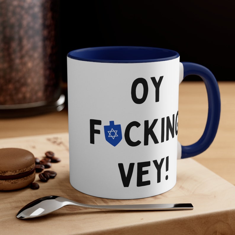 Puede incluir: Taza de caf&eacute; de cer&aacute;mica blanca con borde y asa azules. La taza tiene una estrella de David negra y el texto "OY F*CKING VEY!" impreso en ella.