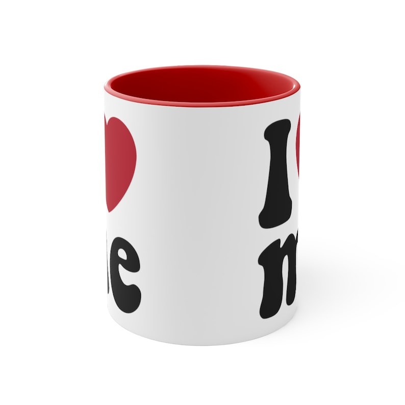 May include: White ceramic mug with a red rim. The mug has a black heart with the word "me" and a black "I" with a red heart next to it.