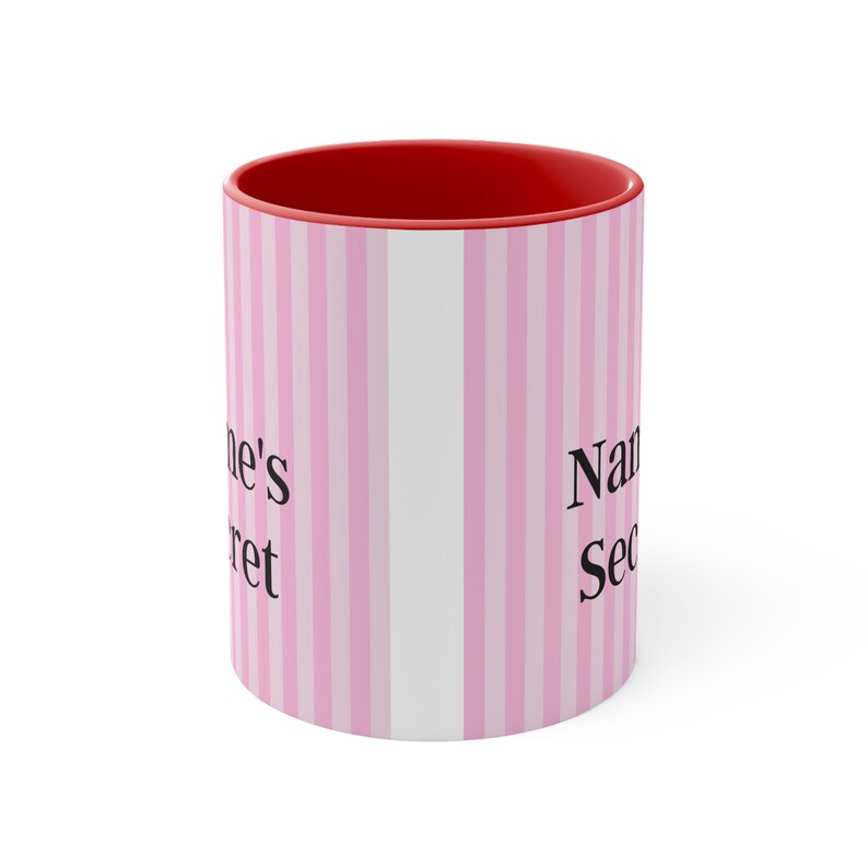 May include: A pink and white striped ceramic mug with a red rim. The mug has the text "Name's Secret" printed on it.