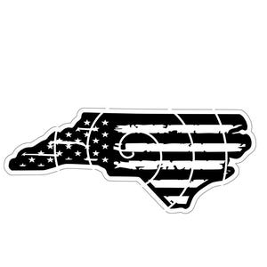 May include: A black and white sticker in the shape of North Carolina, with an American flag design. The sticker has a distressed appearance with white stars and stripes. The Lazy Bear Hat Co. logo is in the upper left corner.