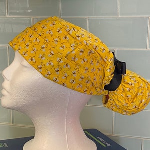 Könnte beinhalten: Eine gelbe OP-Mütze mit Bienenmuster und einem schwarzen Band. Die Mütze sitzt auf einem weißen Mannequin-Kopf.