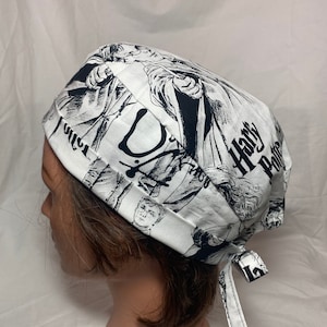 May include: White and black patterned scrub cap featuring illustrations and the words "Harry Potter." The cap is tied at the back with matching fabric ties. The design includes various character images and text.