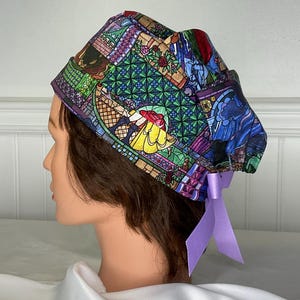 May include: A colorful scrub cap featuring a stained-glass design with images of a princess in a yellow dress. The cap has a purple ribbon tied at the back. The cap is designed for medical professionals.