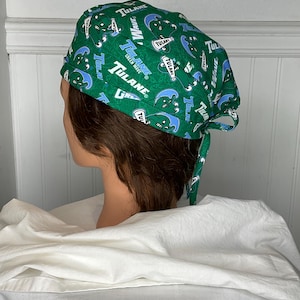 Può includere: Cappello chirurgico verde con un motivo blu e bianco dell'Università di Tulane. Il cappello è legato sul retro ed è esposto su una testa di manichino.