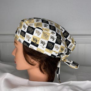 May include: A black, white, and gold patterned scrub cap. The cap features a repeating checkerboard design with the letters "WF" in each square. The cap is tied at the back with matching fabric ties.