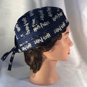 May include: A dark blue head wrap featuring the words "Harry Potter" in white, with a houndstooth pattern. The head wrap is tied at the back and is displayed on a mannequin head.