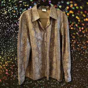 Pode incluir: Uma camisa de botões de manga comprida com padrão de pele de cobra em dourado e marrom. A camisa tem gola e fecho de botões.