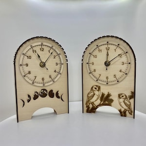 May include: Two wooden clocks with a minimalist design. The clock on the left has a moon phase design and the clock on the right has a bird design.