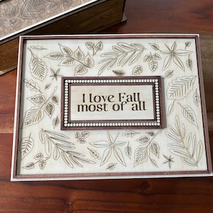 Puede incluir: Una caja de madera con un acabado marrón claro y un diseño decorativo de hojas y el texto "Me encanta el otoño más que nada".