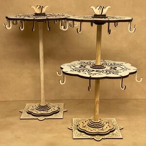 Può includere: Due porta orecchini in legno con intricati disegni tagliati al laser. I porta orecchini hanno più ganci per appendere gli orecchini e presentano una parte superiore decorativa con un motivo floreale.