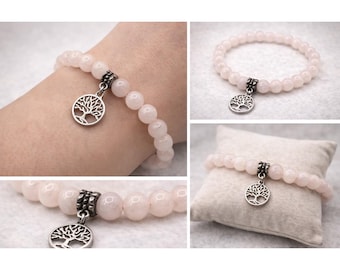 May include: A rose quartz beaded bracelet with a silver-colored tree of life charm. The bracelet is made of small, round, light pink beads. The charm is a detailed, openwork design of a tree.