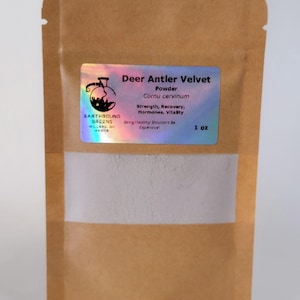 Peut inclure: Un sachet en papier brun avec une fenêtre transparente contenant une poudre blanche. Une étiquette holographique indique "Deer Antler Velvet Powder" avec le texte "Strength, Recovery, Hormones, Vitality". Le sac est étiqueté "Earthbound Greens" et contient 28 grammes de produit.