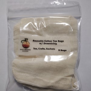 May include: A clear plastic bag containing five reusable cotton tea bags with drawstrings. The bags are off-white and have a label that reads "Reusable Cotton Tea Bags w/ Drawstring" and "Tea, Crafts, Sachets". The brand name "EARTHBOUND GREENS" is also visible.
