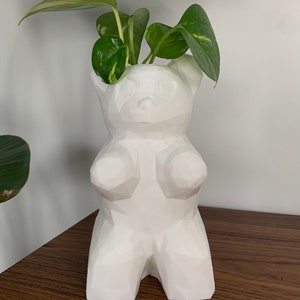 May include: White geometric bear planter with a green plant inside. The planter is made of ceramic and has a matte finish.