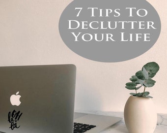 Może przedstawiać: Szare koło z tekstem "7 Tips To Declutter Your Life" na białej ścianie. Laptop z czarną naklejką z napisem "oh la la" znajduje się na białym marmurowym blacie. Na blacie stoi mały wazon z zieloną rośliną.