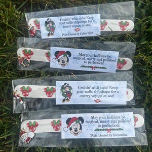 May include: Four nail files in clear plastic sleeves, each featuring a red and green Minnie Mouse icon pattern. Each file includes a small metal charm and a paper label with holiday-themed text and illustrations of Minnie Mouse in a Santa hat.