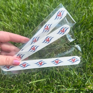May include: White nail files with a repeating pattern of red Mickey Mouse heads and blue wave designs. The files are rectangular and packaged in clear plastic. The background is green grass.