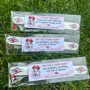 May include: Three nail files in clear packaging, each with a Minnie Mouse design and a charm. The text reads "Cruisin' with style!" and "Set sail & make waves." The background is green grass.