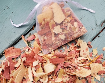 May include: A white mesh bag filled with pink, yellow, and brown wood chips. The bag is sitting on a blue wooden surface, and there are more wood chips scattered around it.