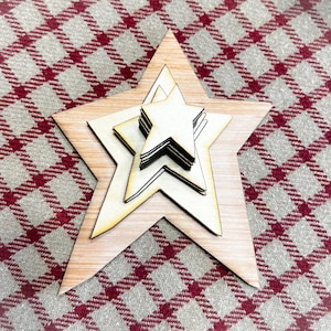 May include: A set of five wooden stars, layered on top of each other, with the largest star at the bottom and the smallest star at the top. The stars are all the same shape and size, but they are different shades of brown. The stars are on a red and white checkered background.