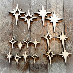 May include: A collection of wooden star ornaments in various sizes, arranged on a rustic wooden background. The stars are all cut from a light-colored wood and have a simple, elegant design.