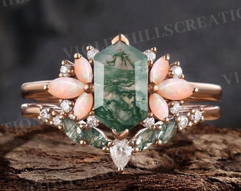 Può includere: Un set di anelli in oro rosa con una pietra centrale esagonale in agata muschiata verde, circondata da opali rosa e dettagli di diamanti. Il set include una fascia abbinata con dettagli di diamanti, perfetto per un fidanzamento o un matrimonio.