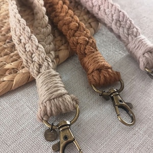 Può includere: Tre portachiavi in corda intrecciata con moschettoni in metallo. I portachiavi sono beige, marrone e marrone chiaro. Il portachiavi beige ha un piccolo cartellino metallico con la scritta "TOME & FICKLE".