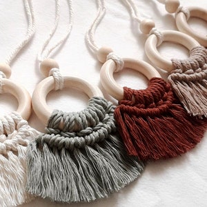 Könnte beinhalten: Fünf hölzerne Ring-Auto-Lufterfrischer mit Makramee-Quasten in den Farben Weiß, Grau, Braun, Beige und Rost. Die Ringe sind an weißen Schnüren befestigt.