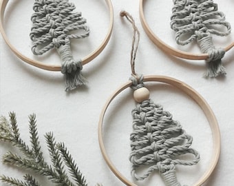 Può includere: Tre ornamenti circolari con alberi di Natale in macramè grigio chiaro centrati in cerchi di legno chiaro. Ogni ornamento include una singola perla di legno naturale sulla parte superiore, un laccio in juta per appenderlo e una nappa.
