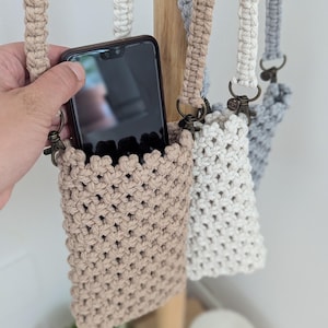 May include: Three crocheted phone pouches with adjustable straps. The pouches are in beige, white, and gray. A smartphone is in the beige pouch.