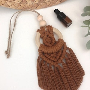 May include: A brown macrame car air freshener with a wooden ring and two wooden beads. The air freshener has a tassel fringe.