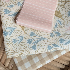 以下が含まれることがあります： 3つの生地見本：薄い青と金の色の花柄がついたベージュの生地、白いストライプのピンクの生地、ベージュと白のギンガムチェックの生地