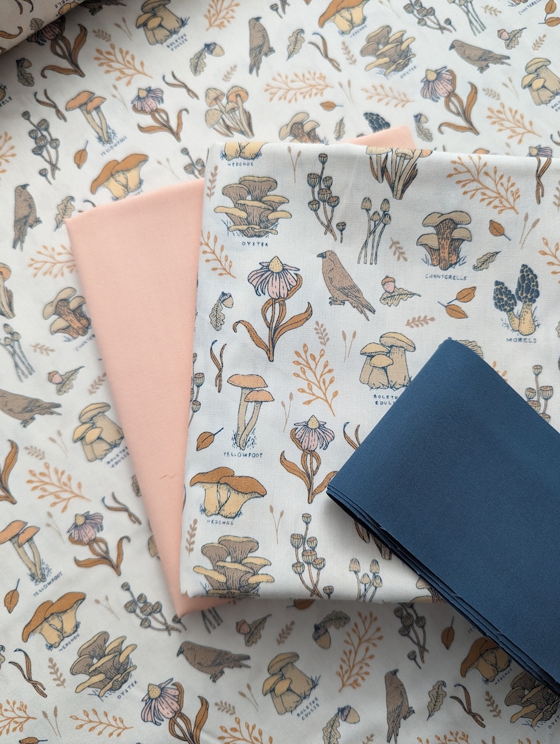 May include: A white fabric with a repeating pattern of mushrooms and birds. The fabric is layered with a pink fabric and a blue fabric.