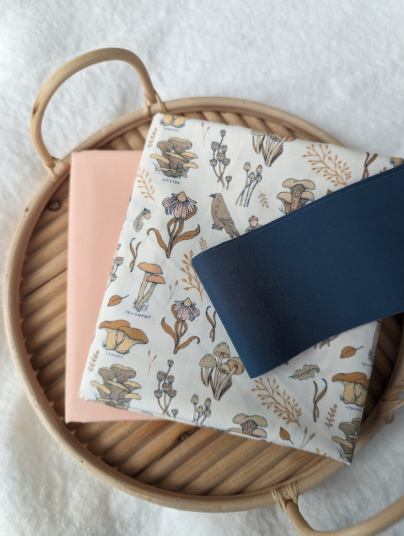 May include: A woven basket tray with a light pink fabric and a white fabric with a mushroom and floral print. The white fabric has the text "Yellowfoot" and "Oyster" printed on it.