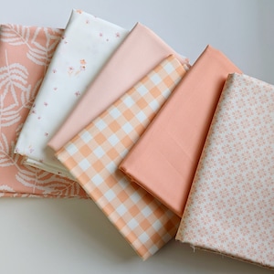 Puede incluir: Un conjunto de seis cuadrados de tela de color melocotón con diferentes patrones, incluyendo hojas, flores, cuadros vichy y un color sólido.