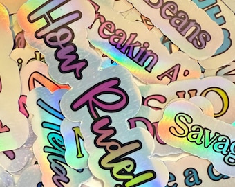 May include: A collection of holographic stickers with various phrases and words in different colors. The stickers have a shiny, iridescent finish and feature phrases like "Cool Beans," "How Rude!," and "Open up a can."