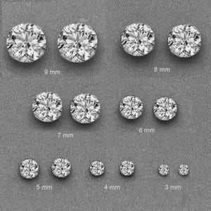 May include: A collection of round, clear gemstone stud earrings in various sizes, ranging from 3 mm to 9 mm. The earrings are displayed on a gray surface, showcasing their sparkling facets. The image highlights the different sizes available.