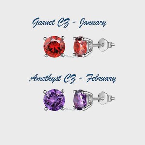 May include: Stud earrings with a round, faceted red garnet CZ gemstone and a silver setting. The text "Garnet CZ - January" is above the earrings. Below are purple amethyst CZ earrings with the text "Amethyst CZ - February".