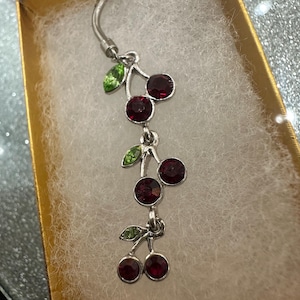 May include: A silver body piercing with a dangling charm of three red cherries with green leaves.