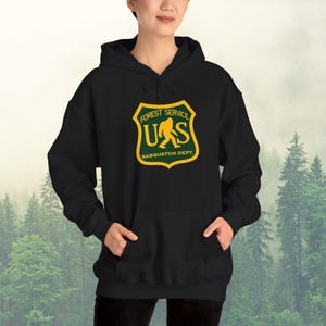May include: Black hooded sweatshirt with a green and yellow graphic of a Bigfoot walking in front of the text "Forest Service US Sasquatch Dept."