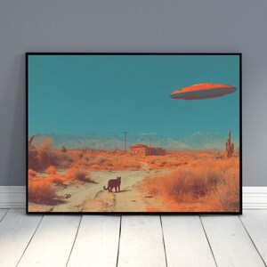 May include: A framed art print depicts a desert landscape under a teal sky. An orange and red flying saucer hovers above. A black cat stands on a dirt road. The scene includes desert plants, a building, and mountains.
