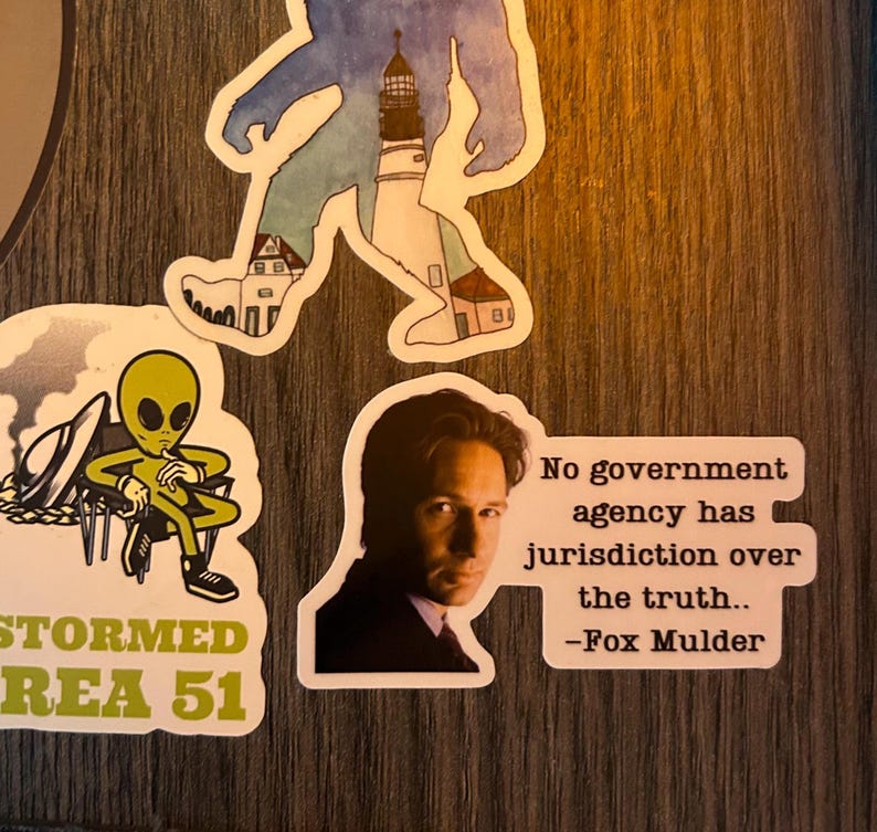 Puede incluir: Una colecci&oacute;n de pegatinas con varios dise&ntilde;os. Una pegatina presenta una silueta de Bigfoot con un faro y edificios. Otra muestra un extraterrestre con el texto "Stormed Area 51". Una tercera pegatina tiene una cita de Fox Mulder.