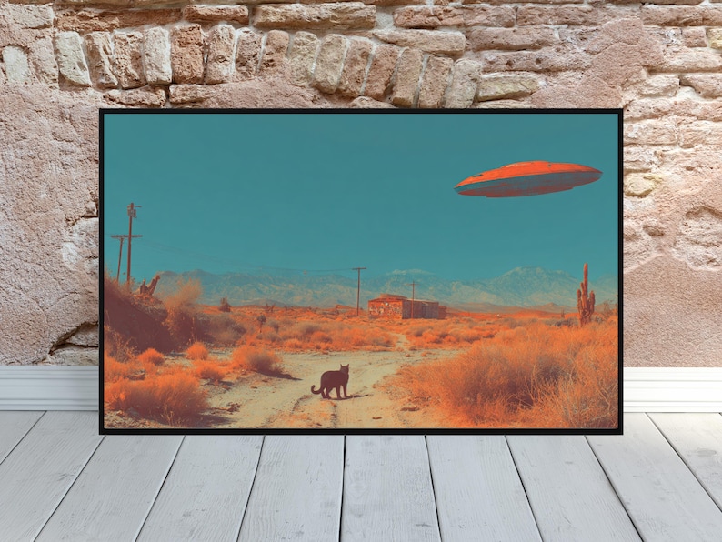 May include: A framed art print depicting a desert landscape under a teal sky. An orange UFO hovers above a dirt road, with a black cat in the foreground. The scene includes cacti, mountains, and a small building, all in warm tones.