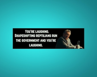 May include: A meme with the text: "YOU'RE LAUGHING. SHAPESHIFTING REPTILIANS RUN THE GOVERNMENT AND YOU'RE LAUGHING." The image shows a man sitting at a table with a mug and a phone.
